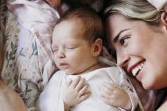 A newborn baby lays sleeping while her parents smile at her.