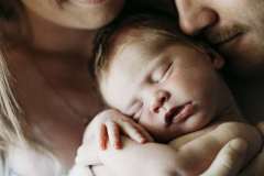 A mother and father gently cuddle their newborn baby in their arms at home in Rockhampton.