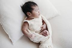 A newborn baby sleeps soundly on a cream cushion in a Rockhampton studio.
