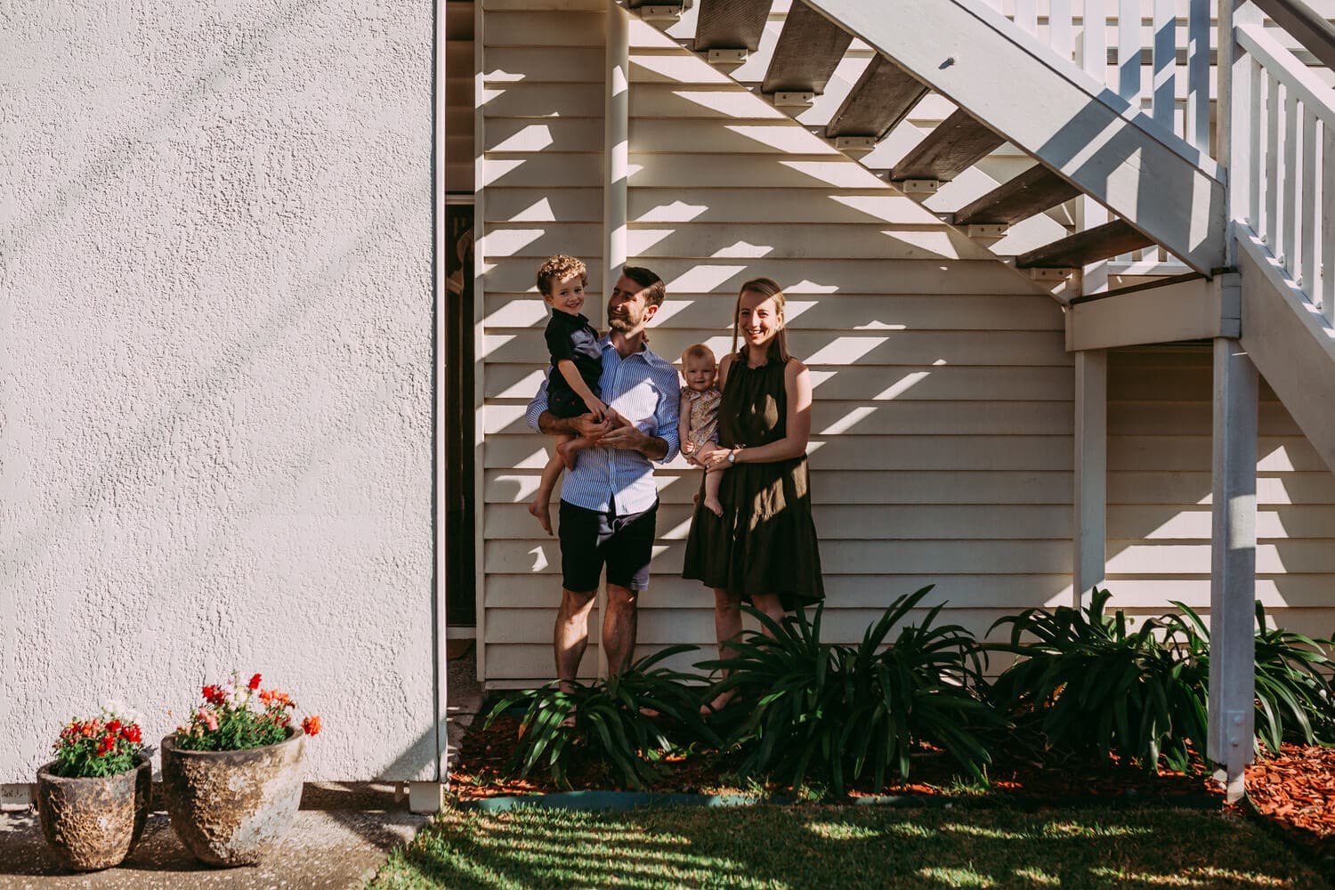 Murphy family A family of four stands under a set of stairs. Light shines through the stairs and casts stripes across the family.