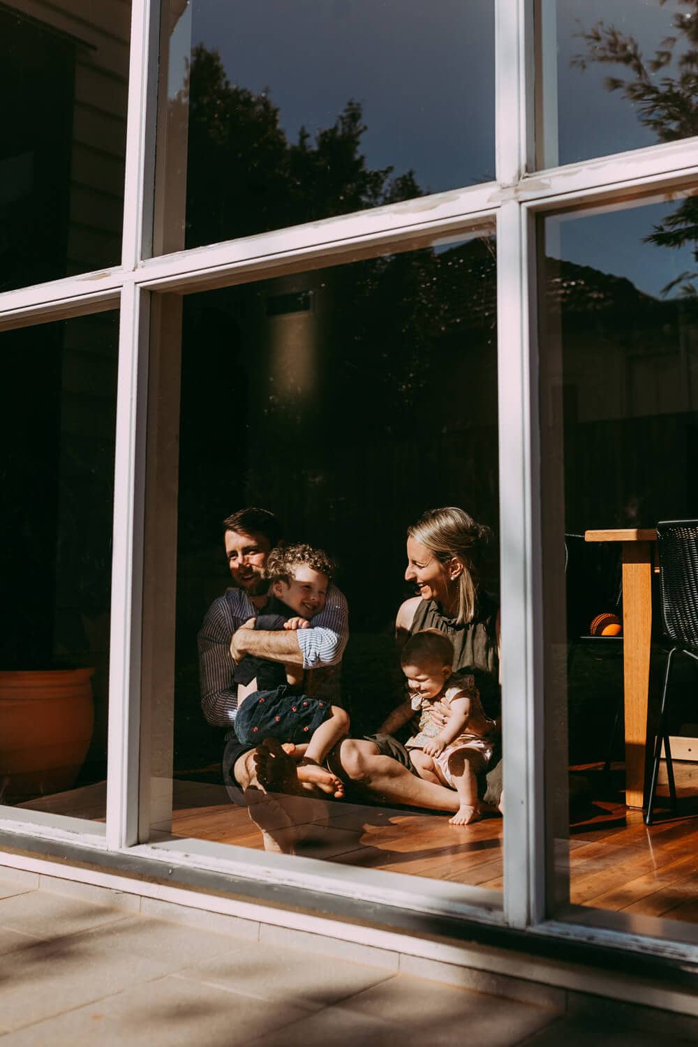 Murphy family Through a big glass window, you can see a family of four cuddling.