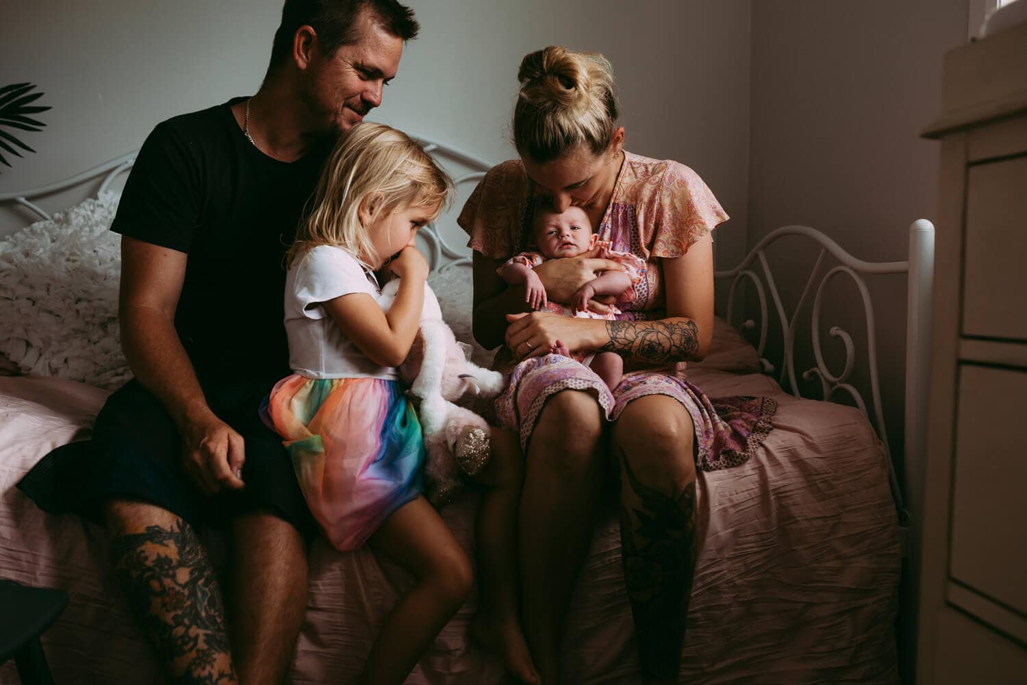 Murphy family A family of four sit on a bed, staring down at their newborn.