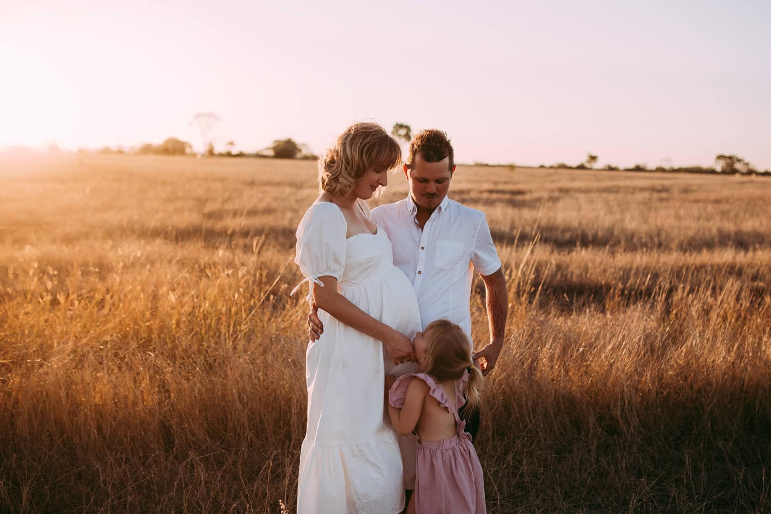 A family of three cuddles as the sun sets