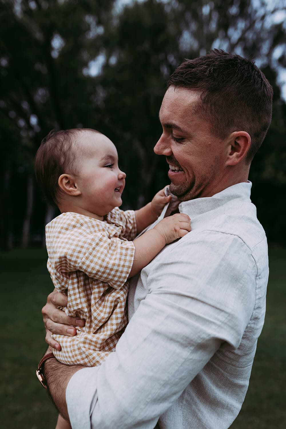 Murphy family A toddler laughs at her father as she holds onto his shirt collar. He smiles back at her.