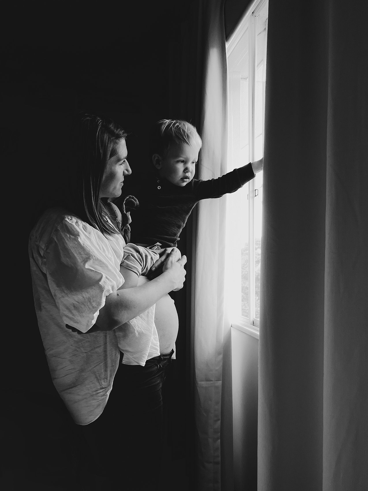 Anna and Baby Hubert 022small A pregnant mother holds her toddler on her belly as they look out a window.