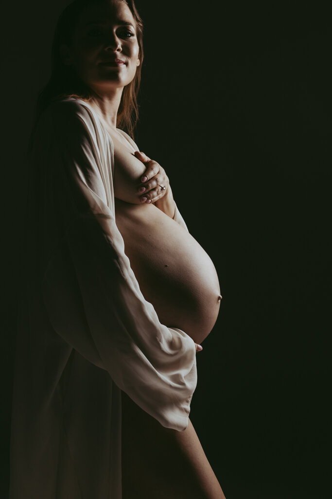 A woman's pregnant belly is illuminated as she looks at the camera.