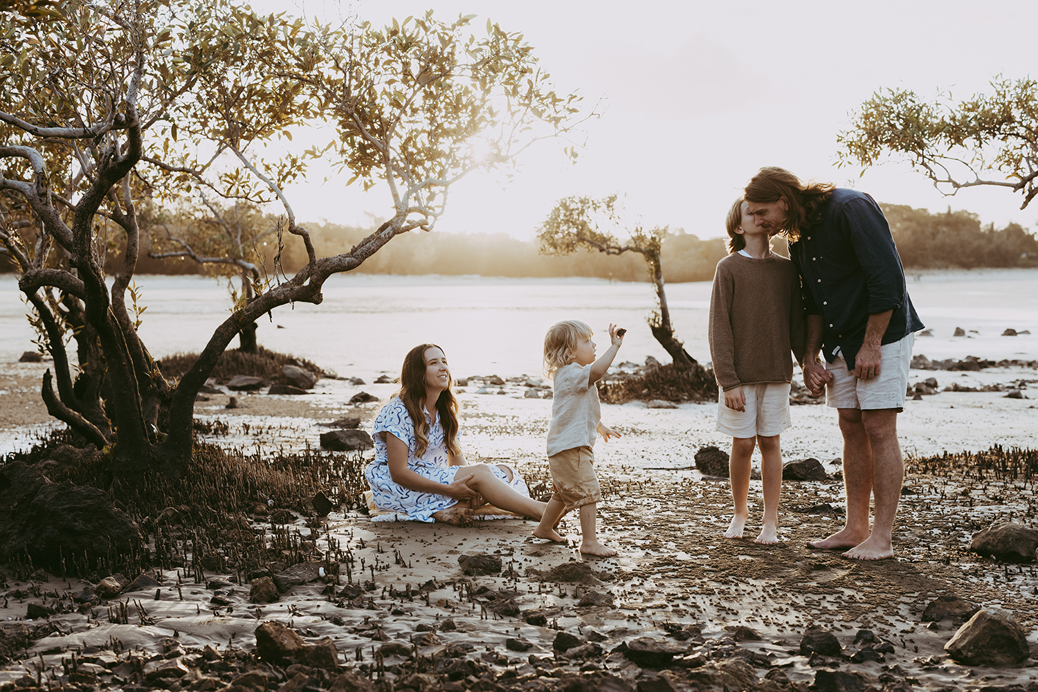 Lucy and Robbie Palmer October 2023 004a_web A family of four is exploring a beach. They are framed by mangroves as the sun sets behind them.