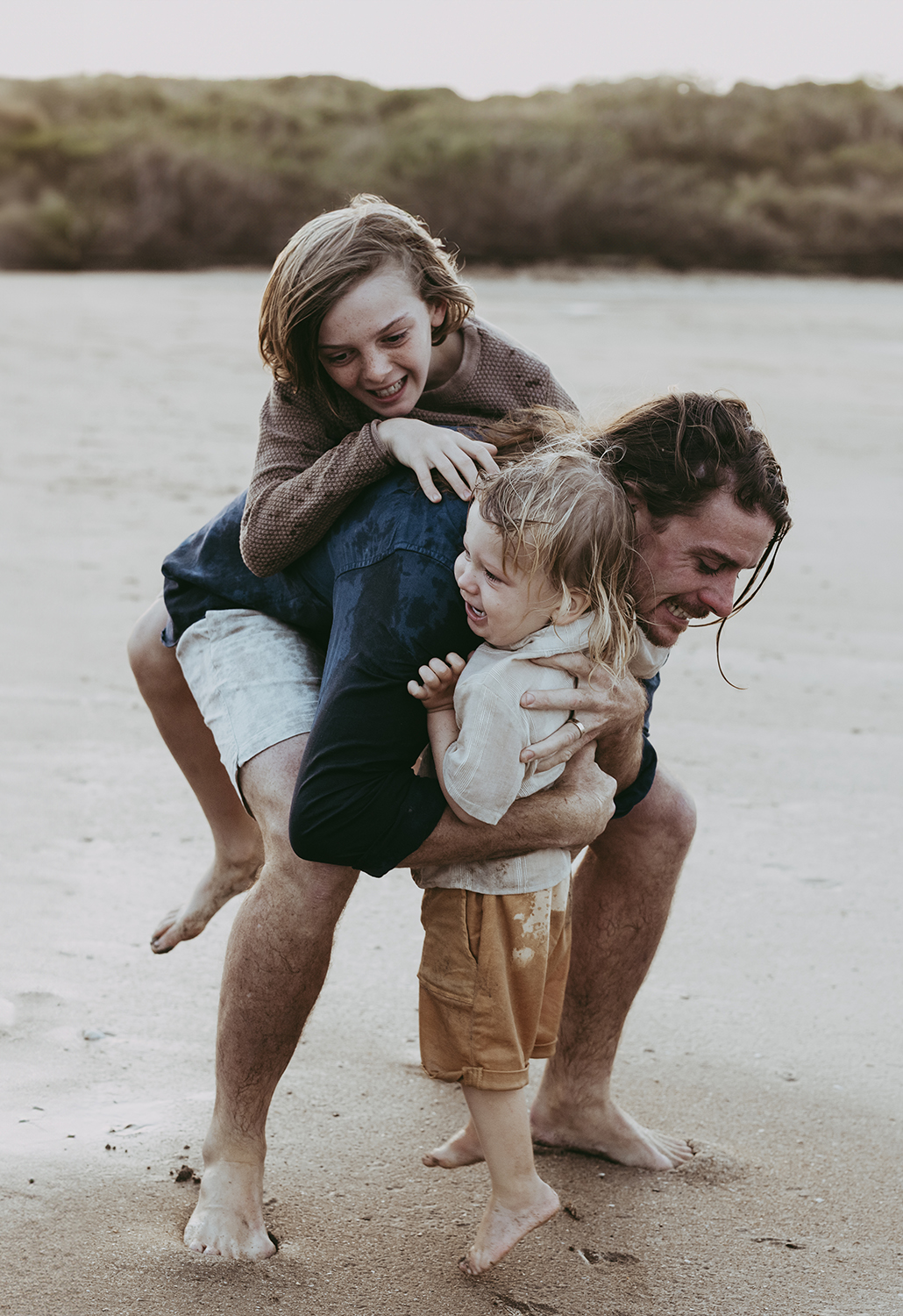 Lucy and Robbie Palmer October 2023 071_web A father cuddles with his two boys on a beach.