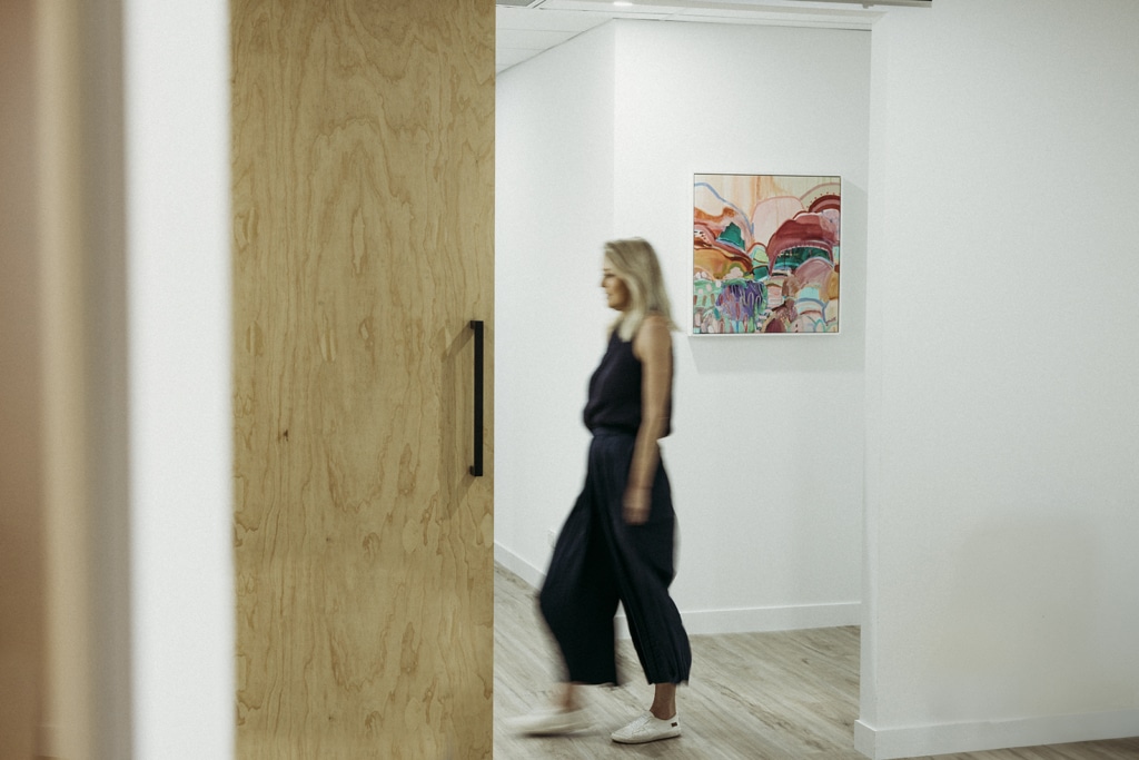A woman is blurred as she walks past a colourful painting.