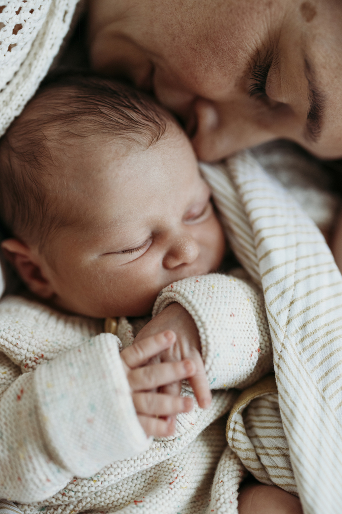A mother snuggles her newborn baby who is wrapped in a warm blanket.