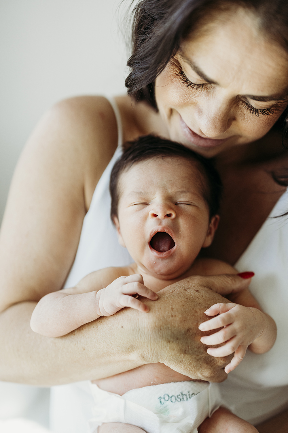 Newborn session A newborn baby is held against his mother's chest as he yawns.