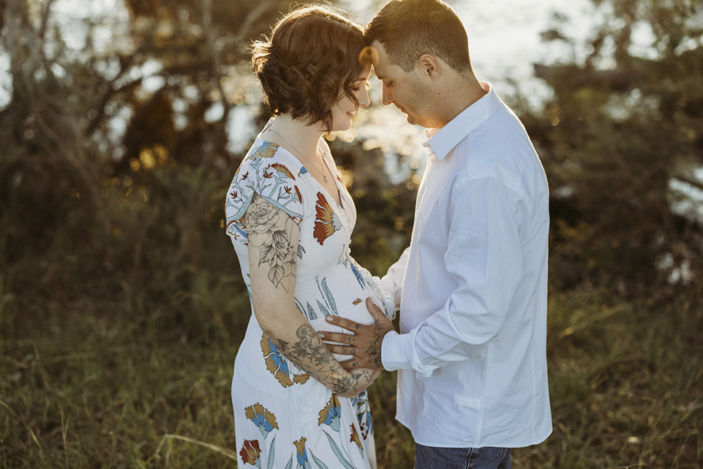 A couple gently place their foreheads together as they both place their hands on the woman's pregnant belly.
