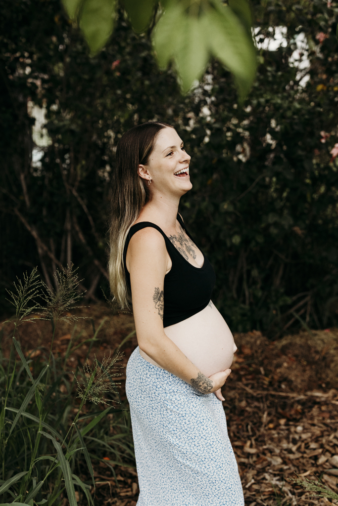 A pregnant mother holds her belly as she laughs.