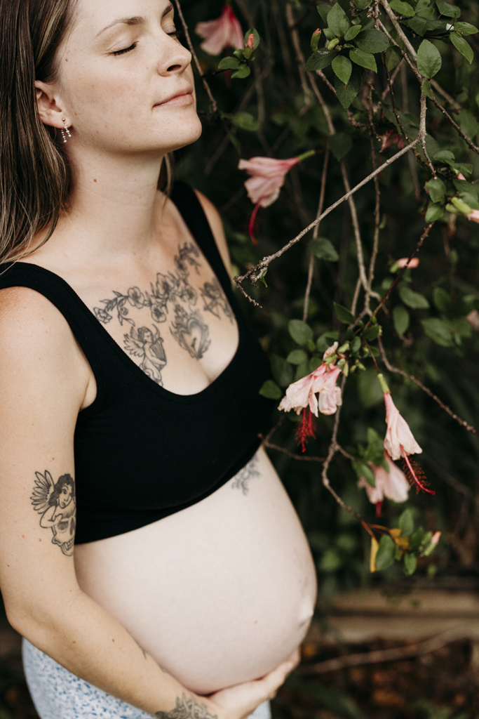A pregnant woman stands in her garden and closes her eyes as she thinks about her baby.