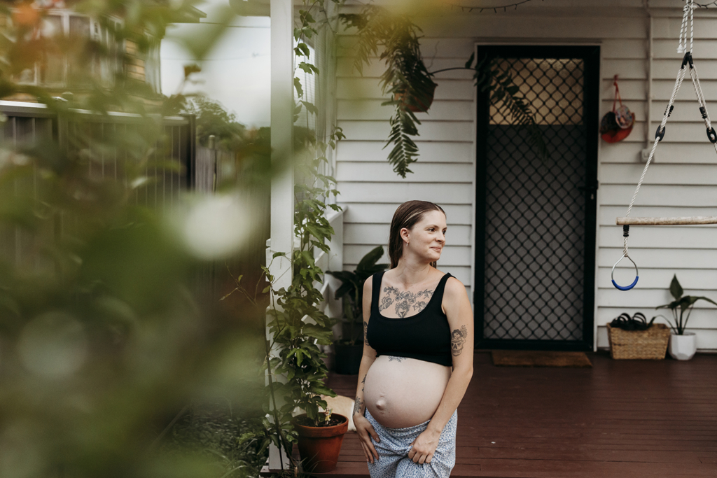 A pregnant mother stands at the front of her home and smiles at her family.