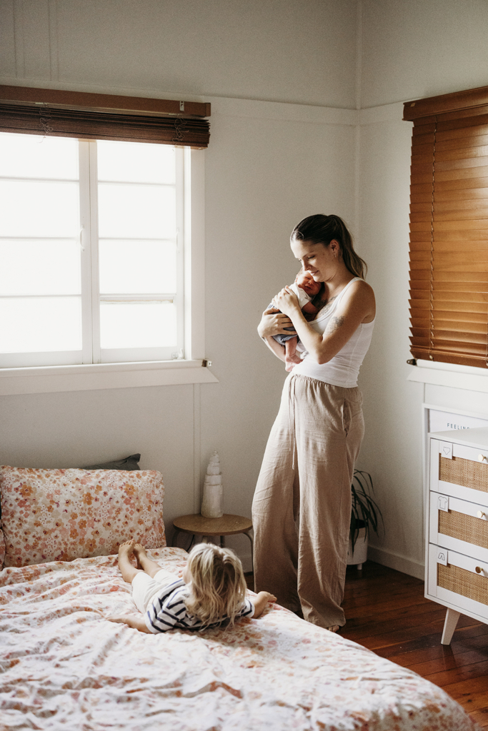 A mother nurses her newborn baby while watching her toddler play next to her.