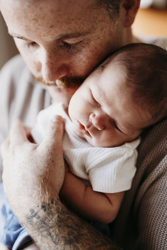 A father cradles his newborn son against his chest.