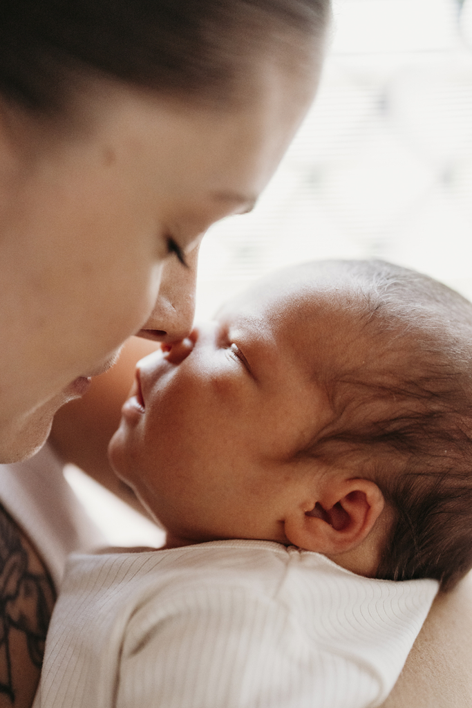 A mother touches her nose to her baby's nose as he sleeps in her arms.
