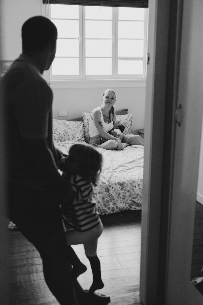 A mother breastfeeds her newborn baby while her husband and toddler look on.