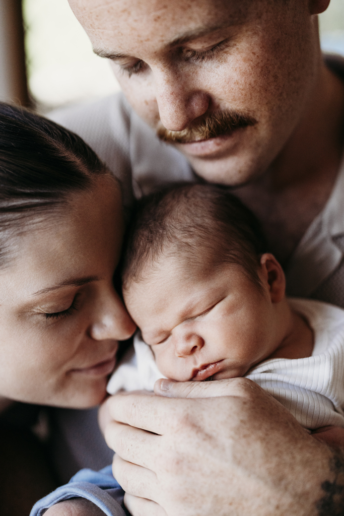 A mother and father cradle their newborn baby.