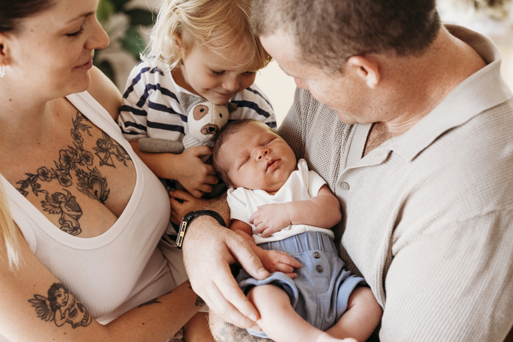A family of four snuggle with their newborn baby.