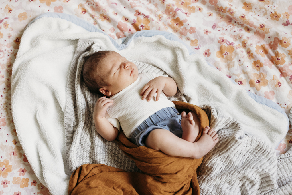 A newborn baby lies on his parents' bed asleep.