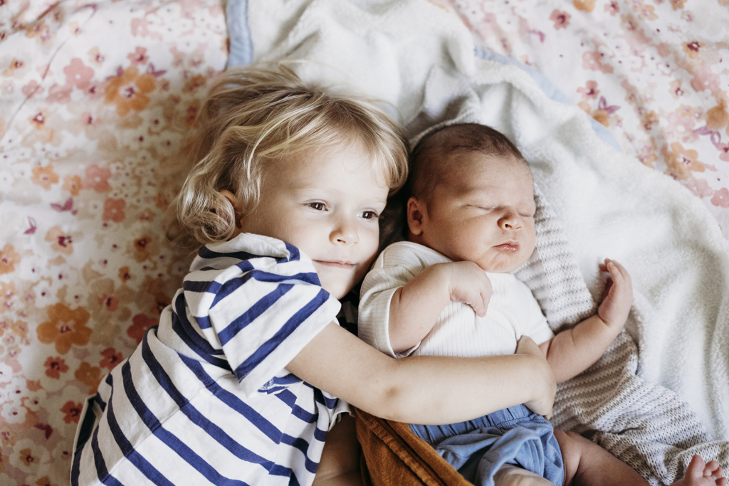 A toddler cuddles her newborn baby brother.