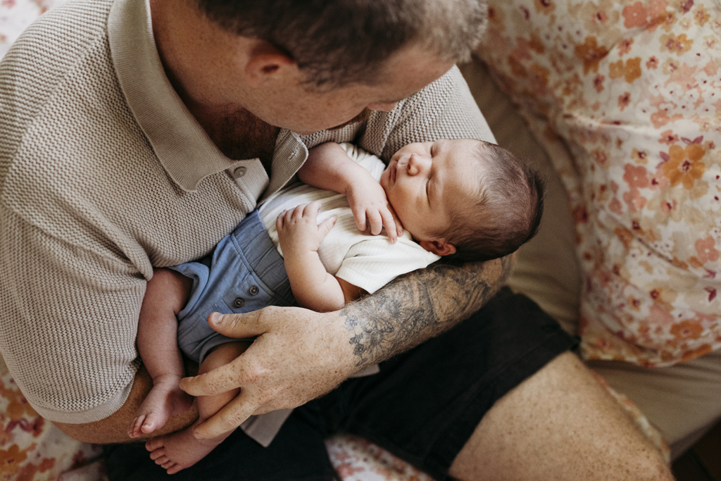A father cuddles his newborn and looks at him in awe.