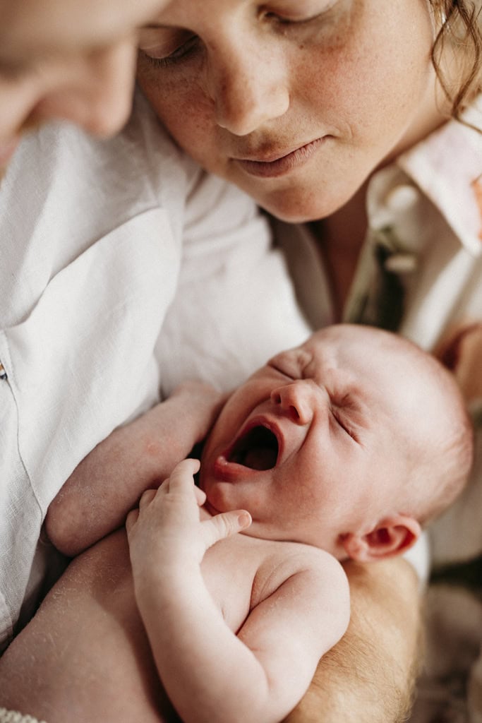 A mother and father hold their newborn baby as she yawns.