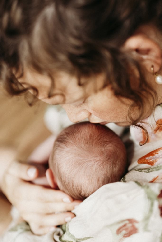 A mother kisses the top of her newborn's head as she lovingly embraces her.
