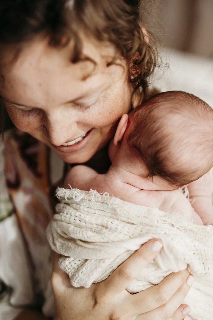 A mother holds her newborn to her chest and smiles.