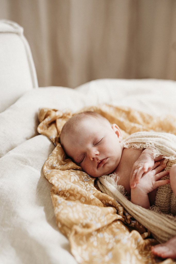 A newborn baby lies in a studio sleeping. She's gently wrapped, with her hands placed on her chest.