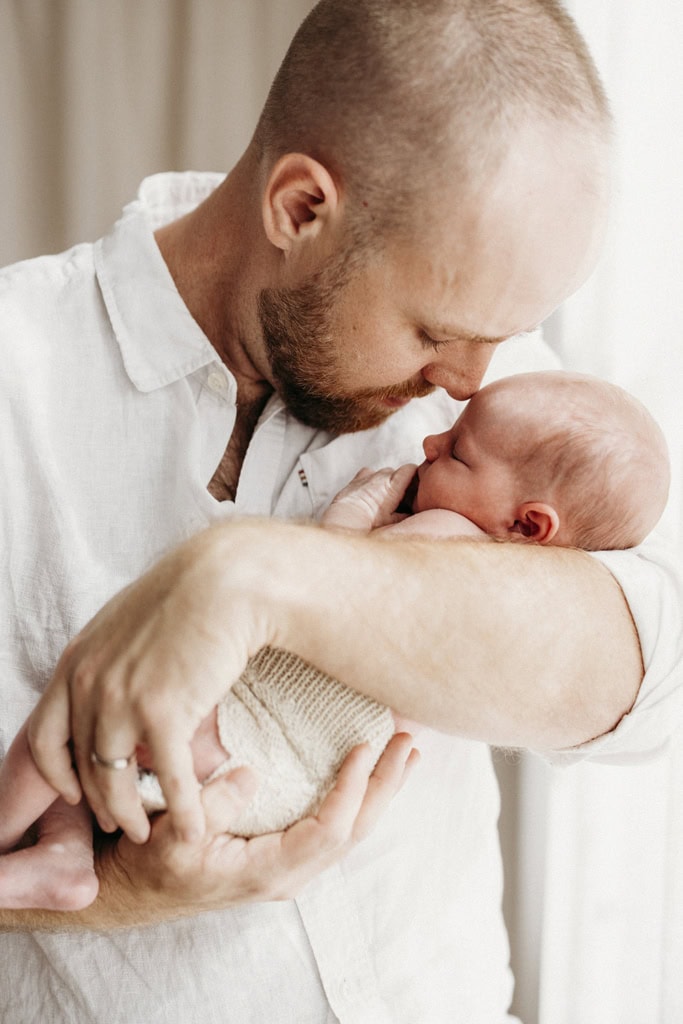 A father holds his newborn baby and gently snuggles her.