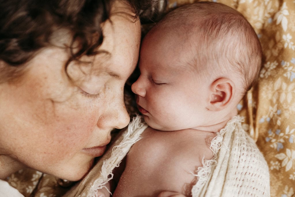 A mother lies next to her newborn baby. Both have their eyes closed.