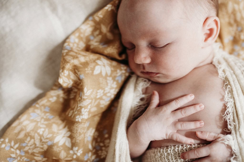 A newborn lays asleep with her hands on her chest.