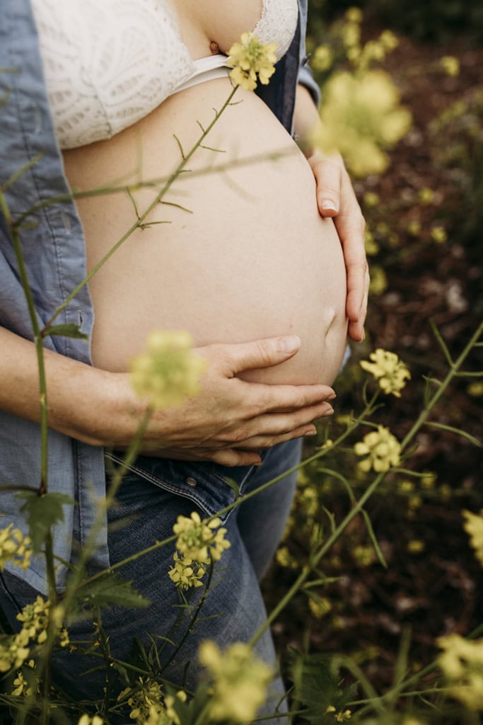 A woman cradles her pregnant belly. Yellow flowers are in the foreground.