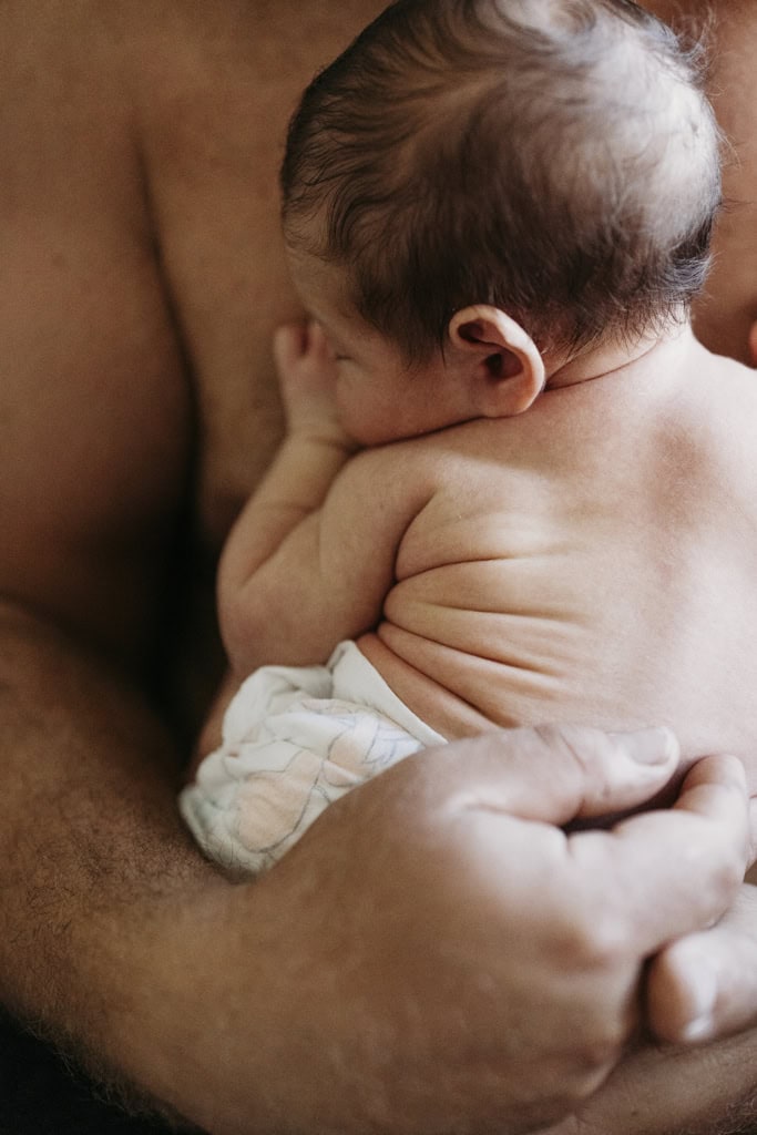 A newborn baby has skin-on-skin time with her father as she snuggles up on his bare chest.