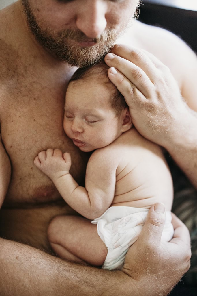 A father cradles his newborn baby on his chest.