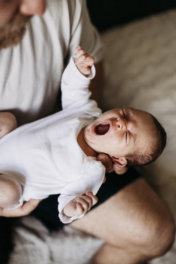 A newborn baby yawns as she's held by her father.