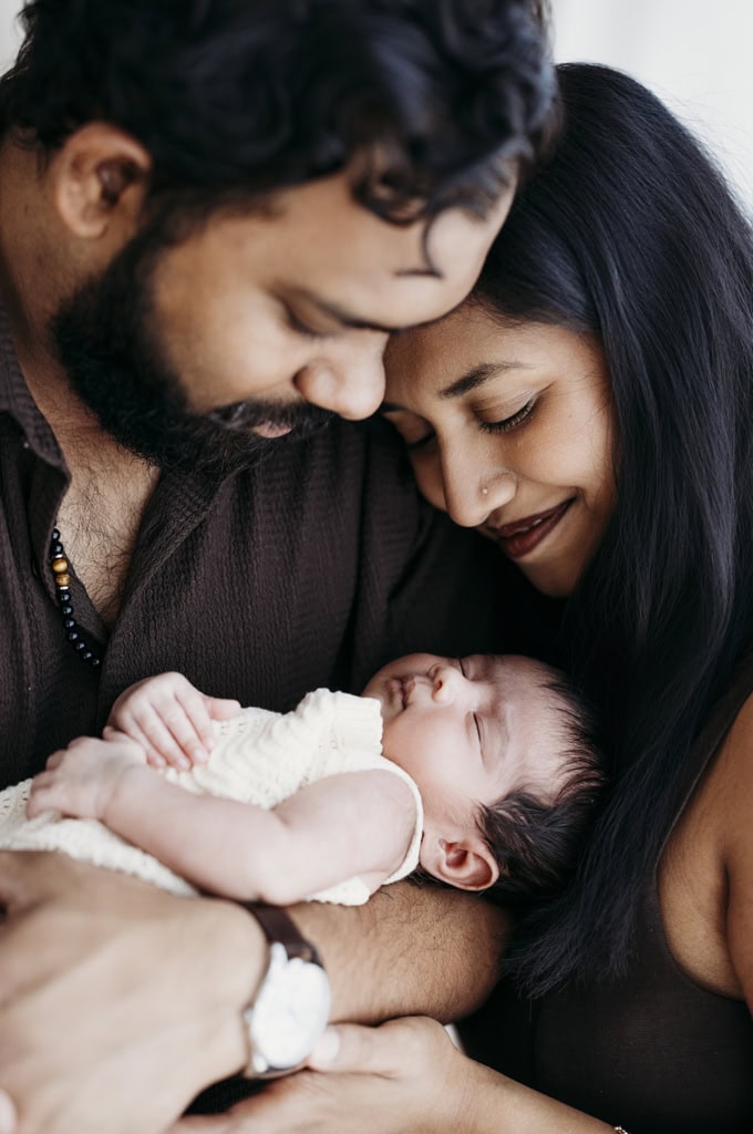 A couple hold their newborn daughter and smile.