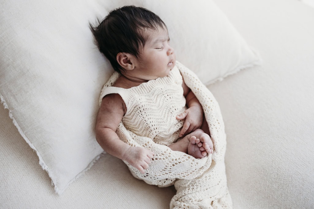 A newborn rests on a linen cushion as she sleeps at a Rockhampton newborn photography studio.