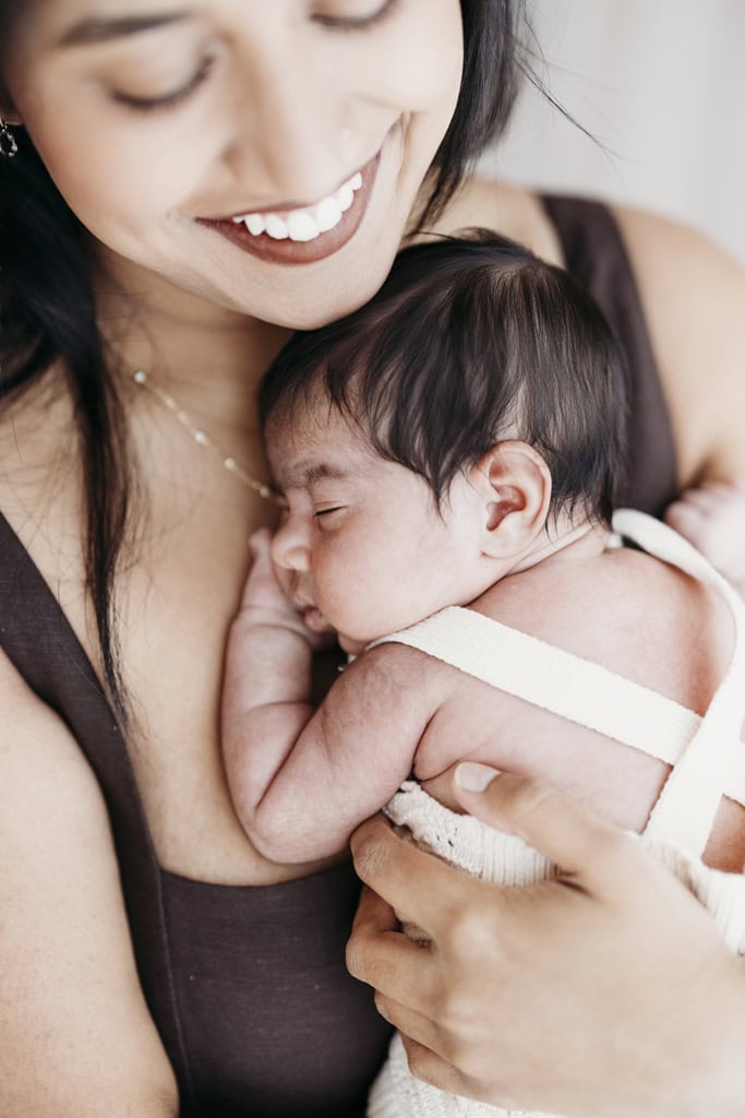 A mother holds her newborn daughter in her arms as she sleeps at a Rockhampton newborn photography studio.