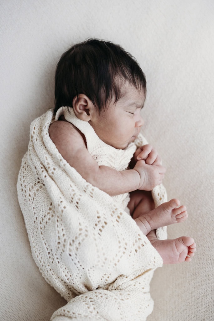 A newborn is snuggled in a blanket as she sleeps.