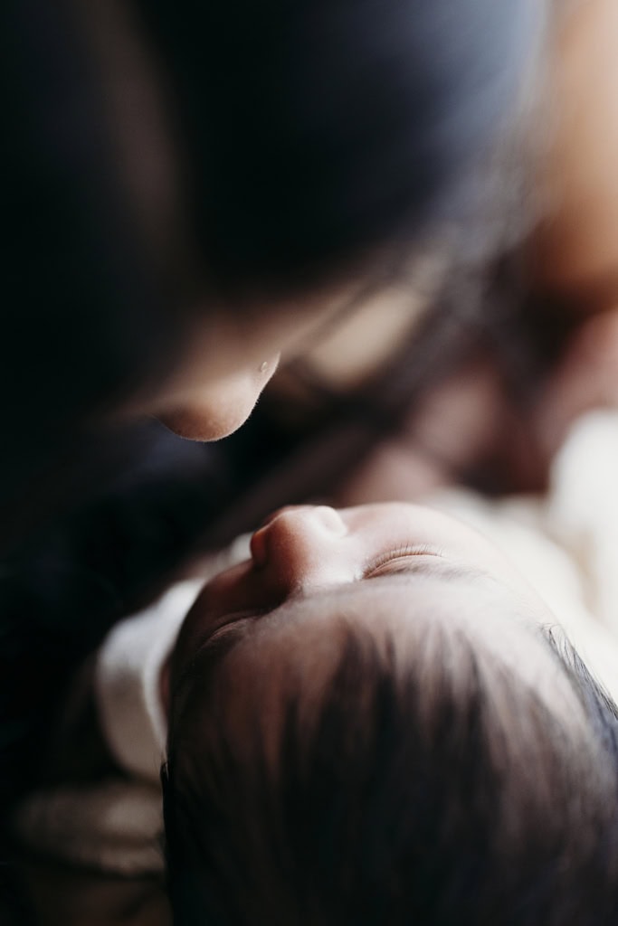 A mother holds her newborn daughter closely as their noses almost touch.
