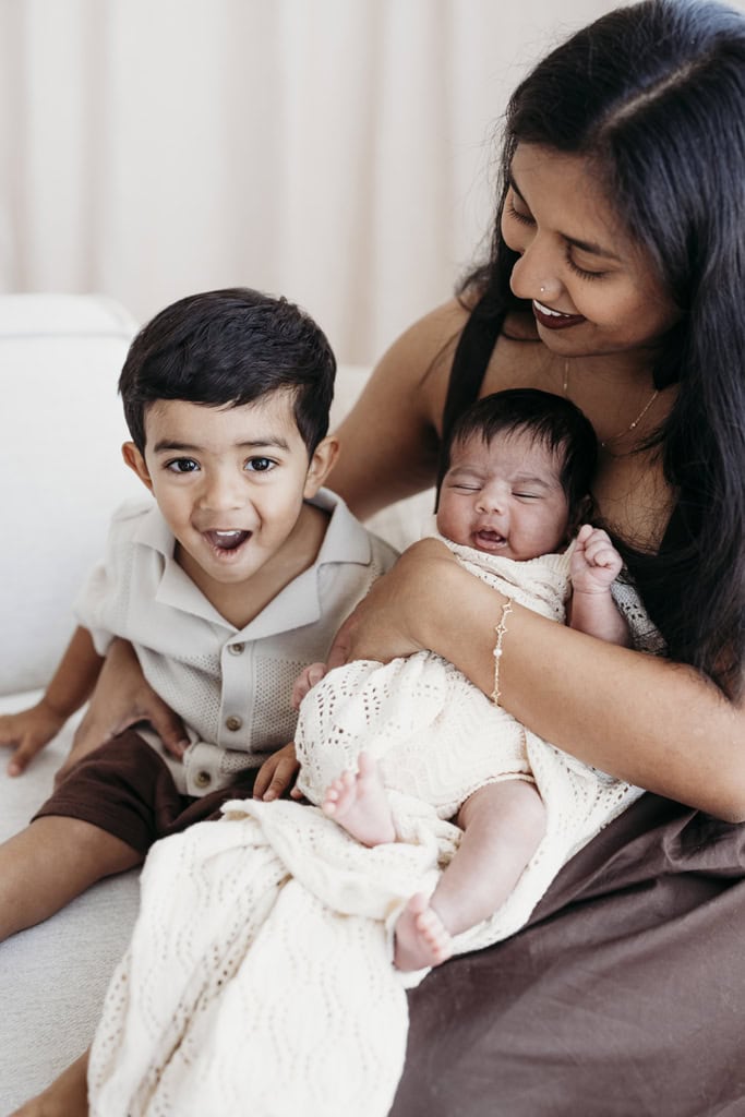 A mother holds her newborn daughter and cuddles her laughing toddler son.