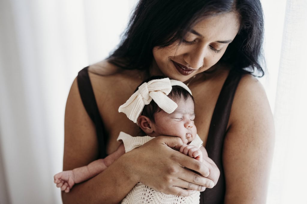 A mother holds her newborn daughter in her arms as she sleeps at a Rockhampton newborn photography studio.