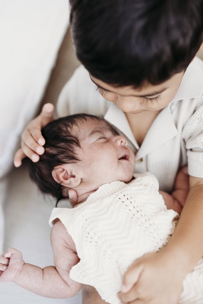 A little boy cradles his newborn sister in his arms at a Rockhampton newborn photography studio.