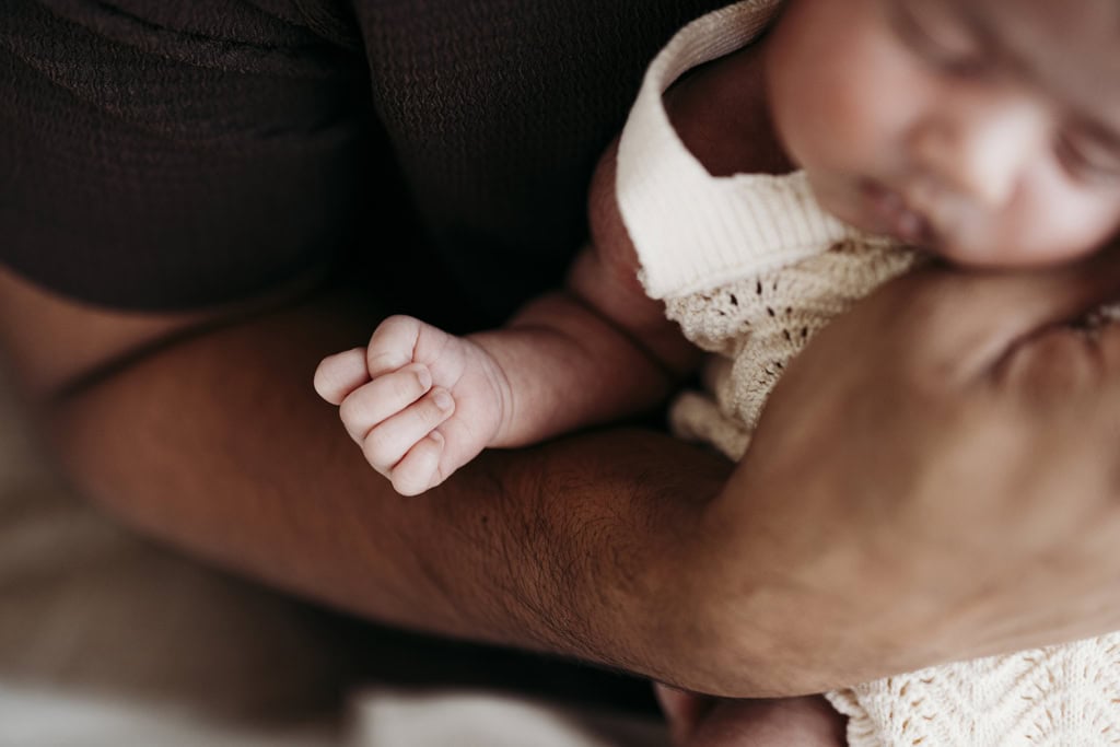 A newborn clenches her fist as she's held in her father's arms at a Rockhampton newborn photography studio.