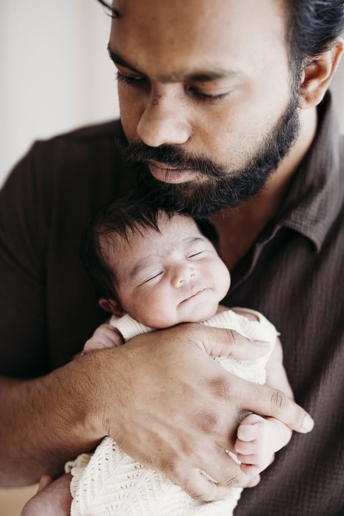 A father holds his sleeping newborn baby against his chest.
