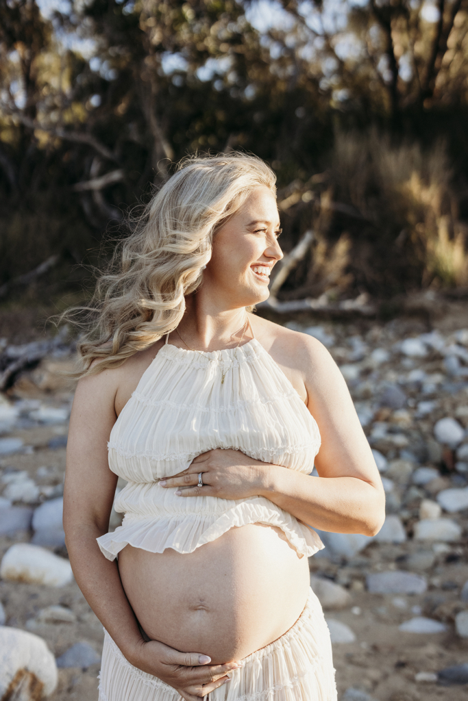 A pregnant woman gently cradles her belly as the sun shines on her skin.
